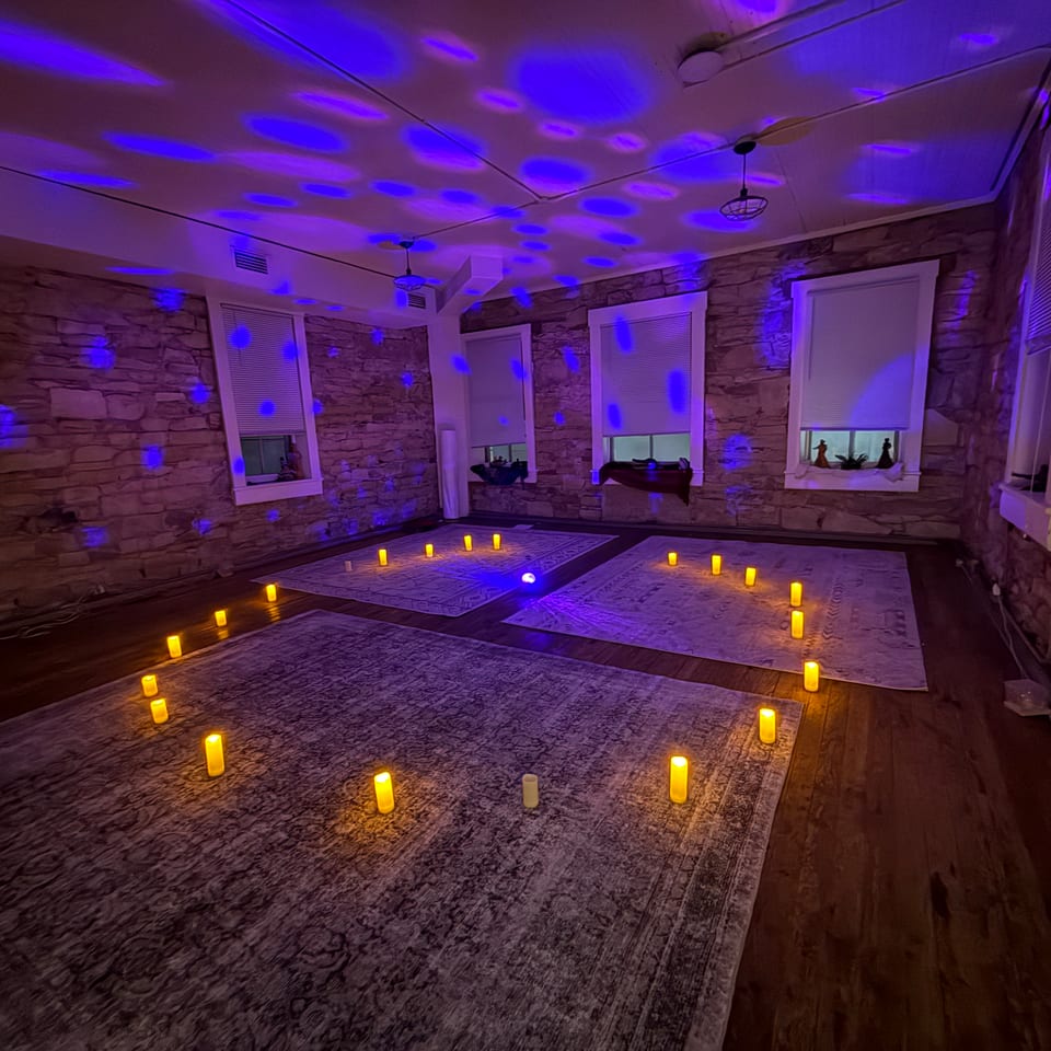 Stone-walled restaurant room with patterned rugs, glowing candles, and blue ambient lighting creating an atmospheric setting.