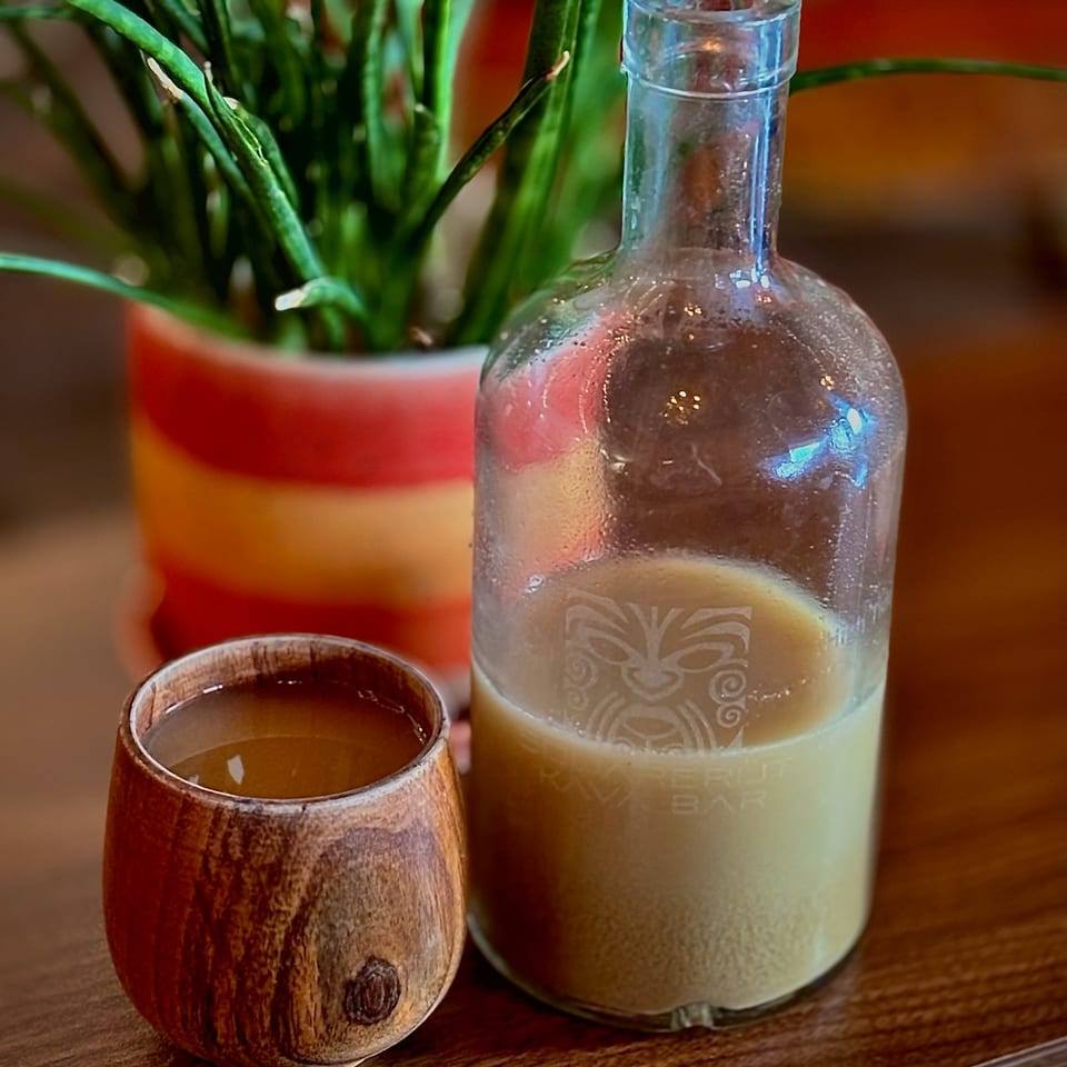Frosted glass bottle and wooden cup of drinks on a restaurant table beside a potted plant.