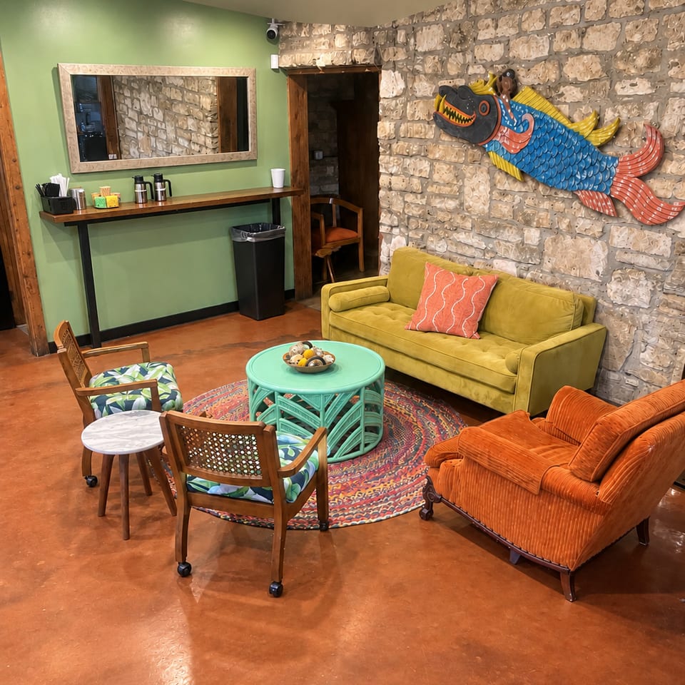 Colorful restaurant lounge with mustard and orange sofas, patterned chairs, a turquoise table, stone walls, and whimsical fish artwork.