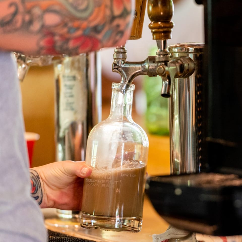 Bartender pours draft beer into a marked glass growler at a busy bar.
