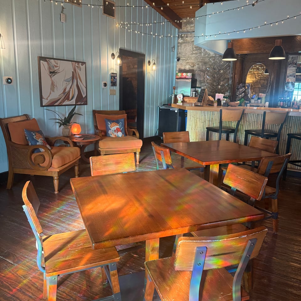 Cozy restaurant interior with wooden tables, chairs, lounge seating, a bar, stone wall, and warm string lights.