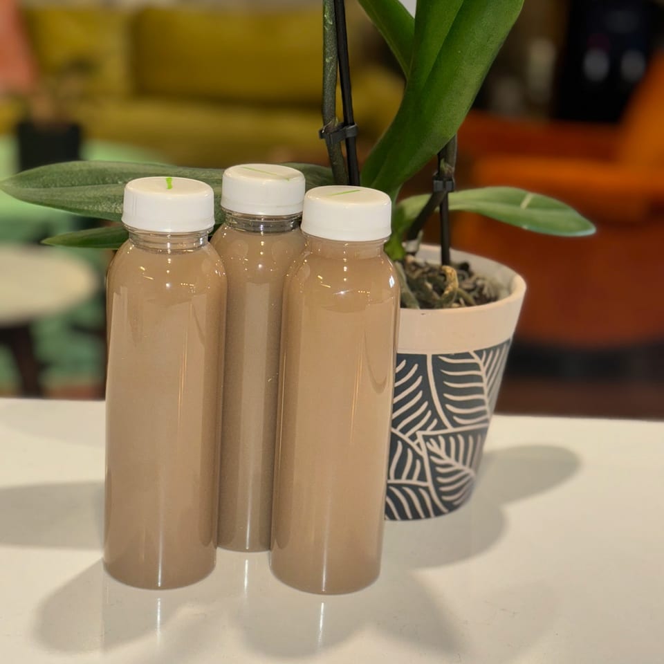 Three bottles of pale beige beverages sit on a counter beside a potted orchid in a warmly lit restaurant.