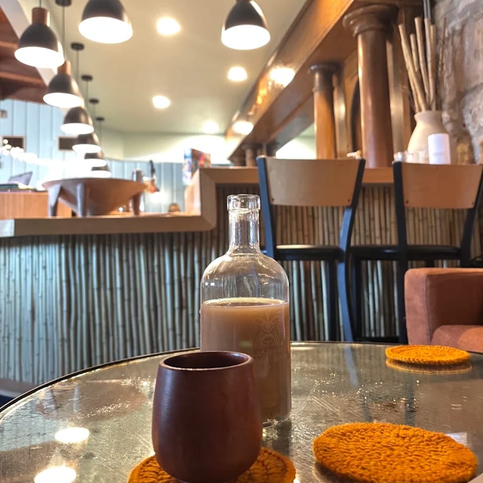 Cozy restaurant interior with pendant lights, a coffee cup, glass carafe, and orange knitted coasters on a table.
