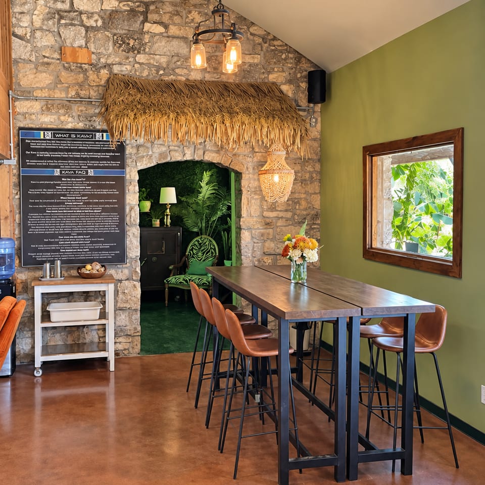 Rustic restaurant interior with stone walls, thatched arch, pendant lights, green accents, and high tables with leather bar stools.